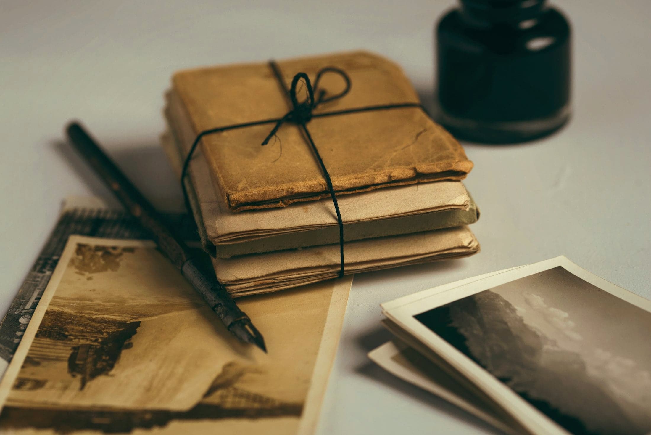A bundle of old papers tied with string, beside a fountain pen and kept photographs
