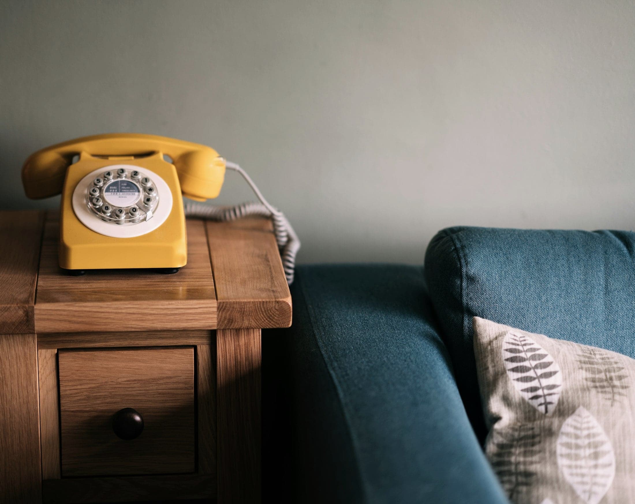 A yellow rotary telephone waiting on a wooden side table beside a sofa